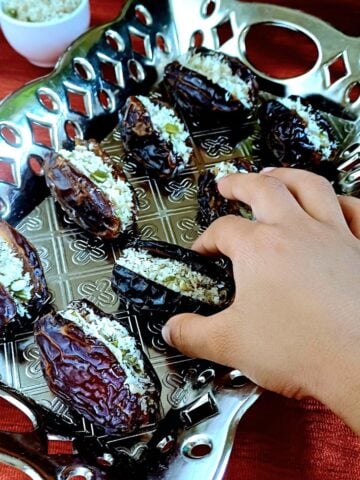 child picking up coconut superseed stuffed dates frorm a plate filled with stuffed dates.