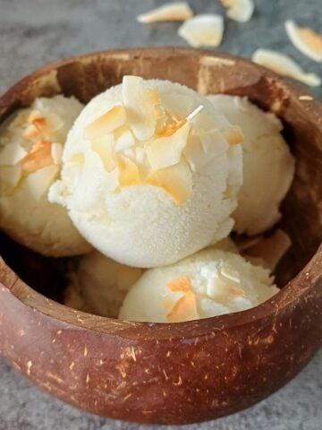 side view of coconut shell with white ice cream scoops topped with toasted coconut flakes.