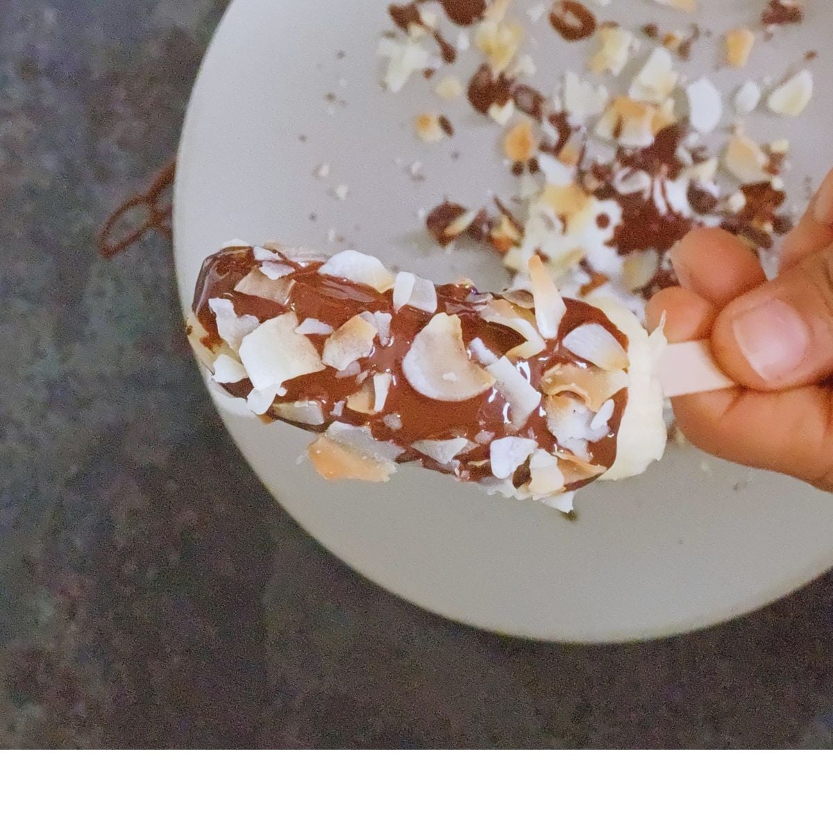 child holding chocolate coated banana topped with toasted coconut flakes.