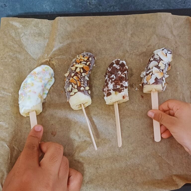 two children holding frozen banana pops placed on lined baking tray.