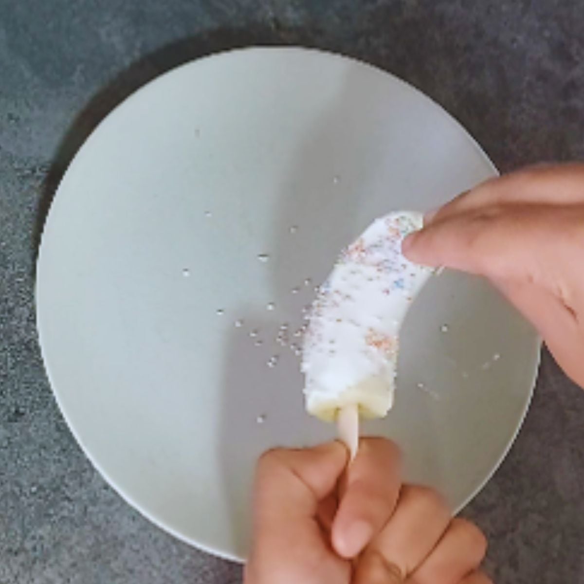 child sprinkling colourful sprinklers on yogurt dipped banana.