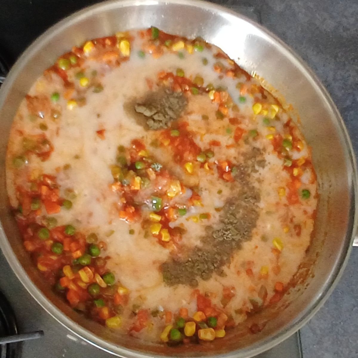 steel pan containing cooked vegetables along with coconut milk and spices.