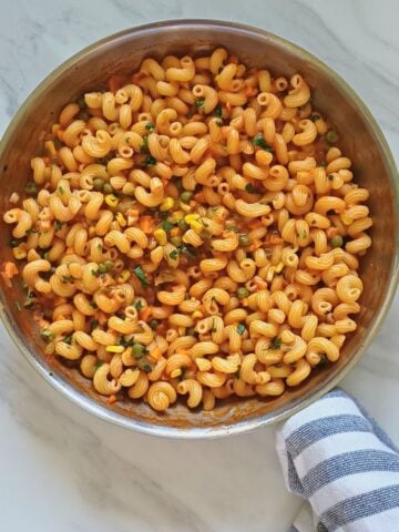 vegetable coconut milk pasta in a steel pan placed on marble with a cloth wrapped around the handle.