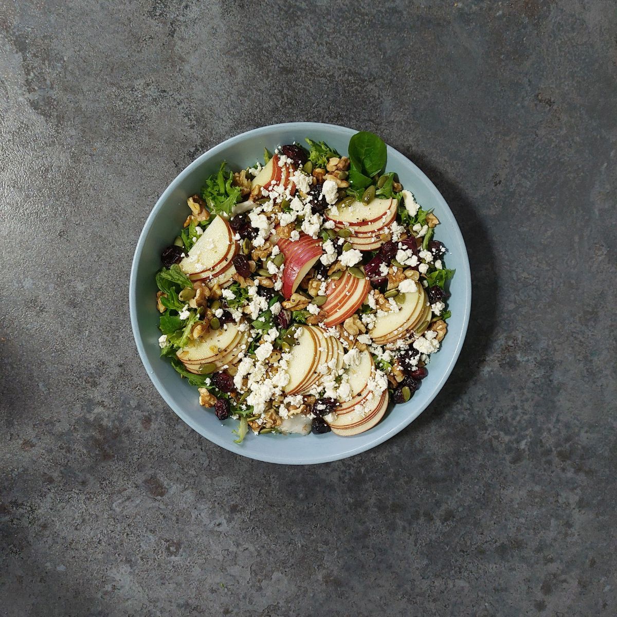 blue bowl of apple walnut feta salad placed on dark coloured platform.