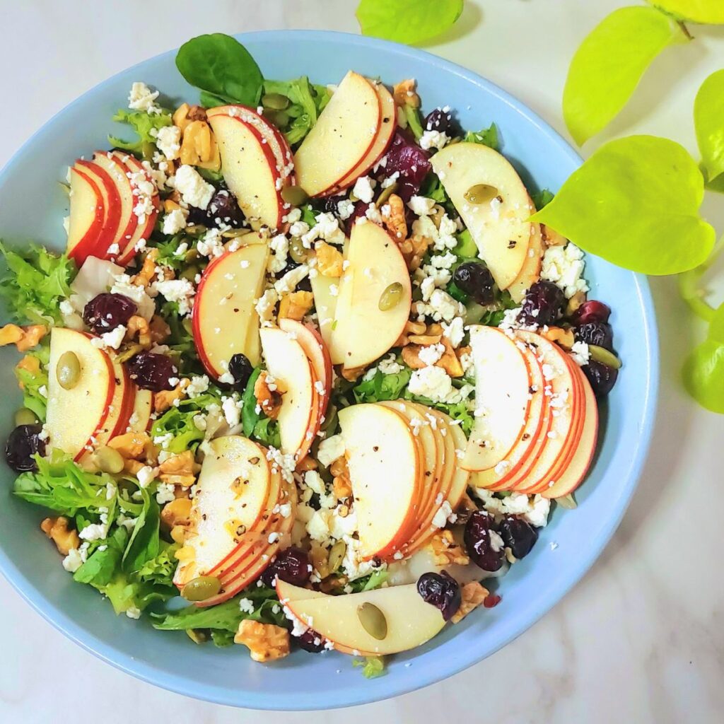 blue bowl of apple walnut cranberries greens salad placed on marble.