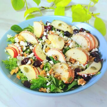 fresh apple greens salad in a blue bowl placed on a marble.