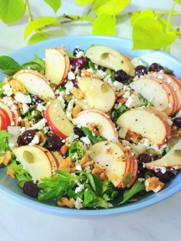 fresh apple greens salad in a blue bowl placed on a marble.