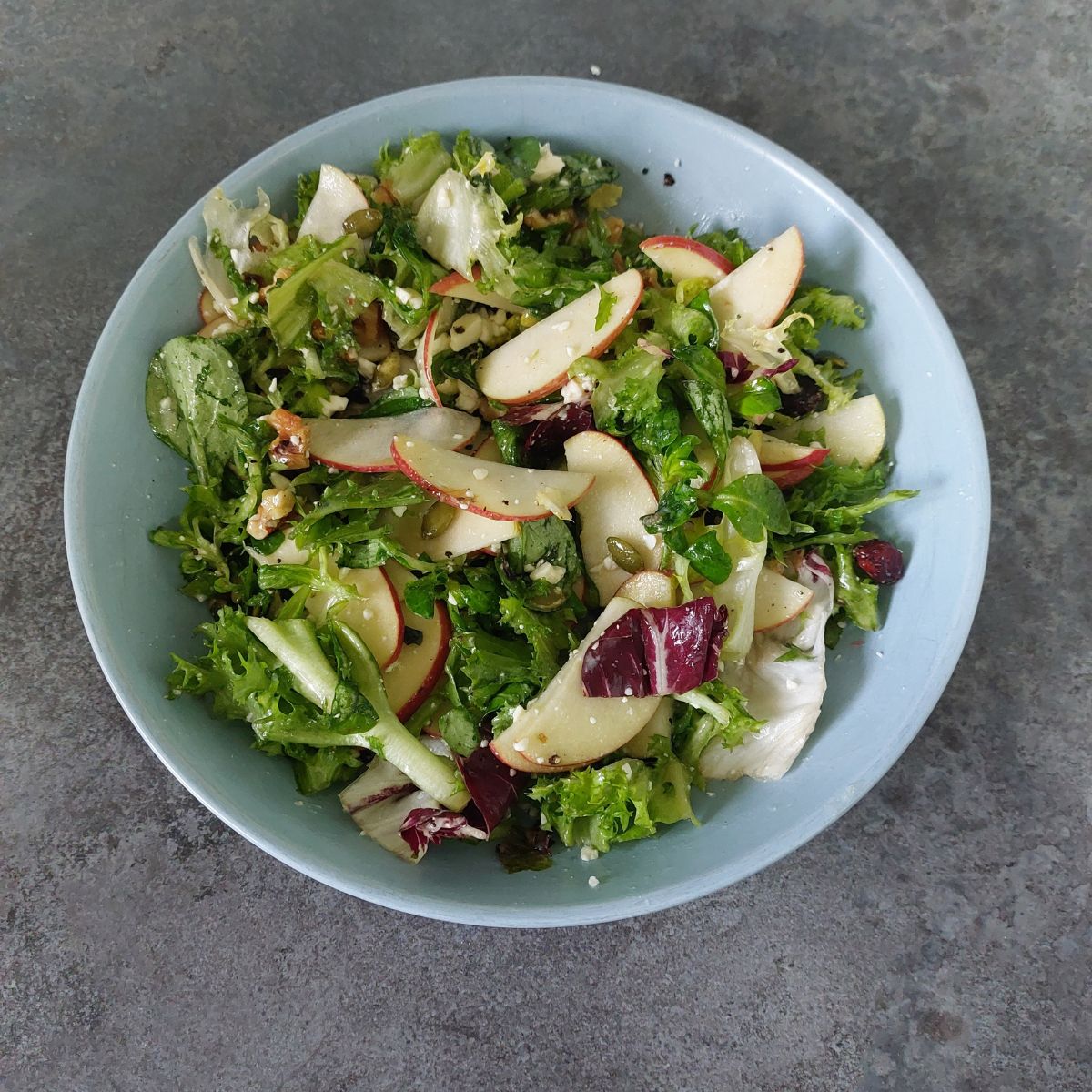 fresh greens, nuts and apple salad in a blue bowl.