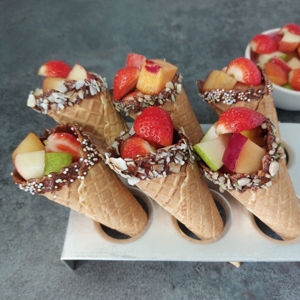 fresh fruits filled in a chocolate coated cones placed inside a cone tray