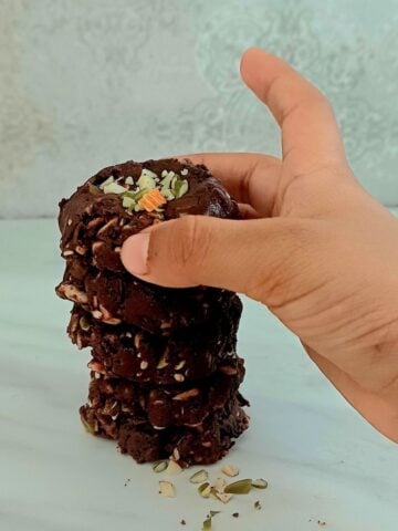 child holding a chocolate superseed bite from a stack of them placed on mrble.