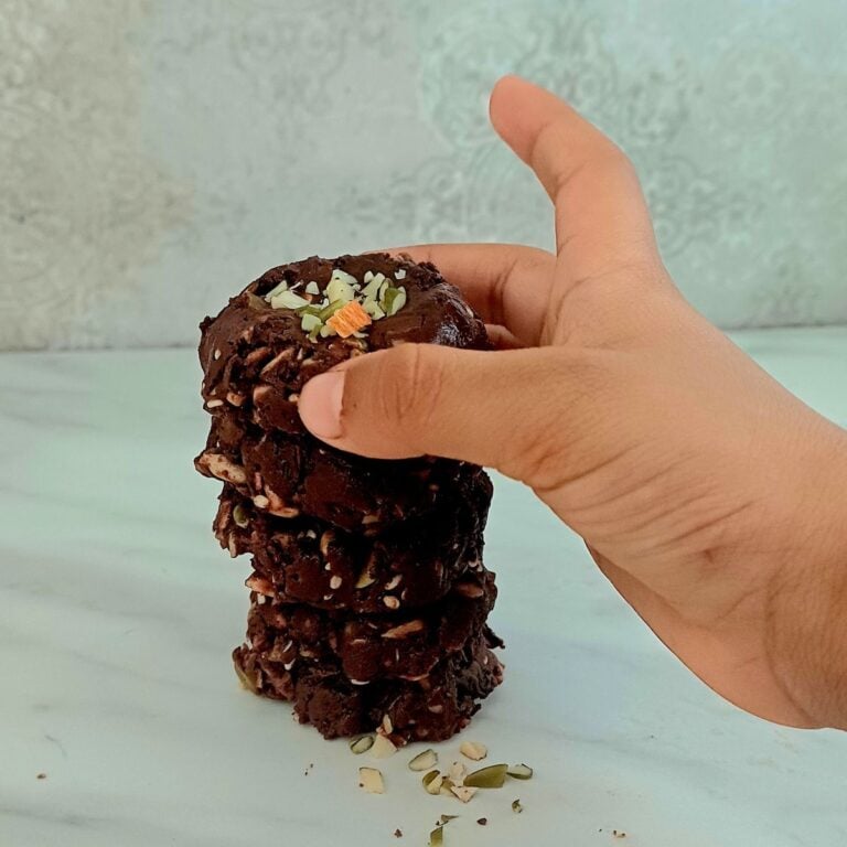 child holding a chocolate superseed bite from a stack of them placed on mrble.