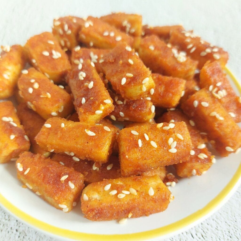 close up image of a white plate of pan fried tofu with sesame seeds.