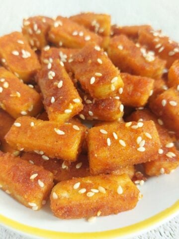 close up image of a white plate of pan fried tofu with sesame seeds.