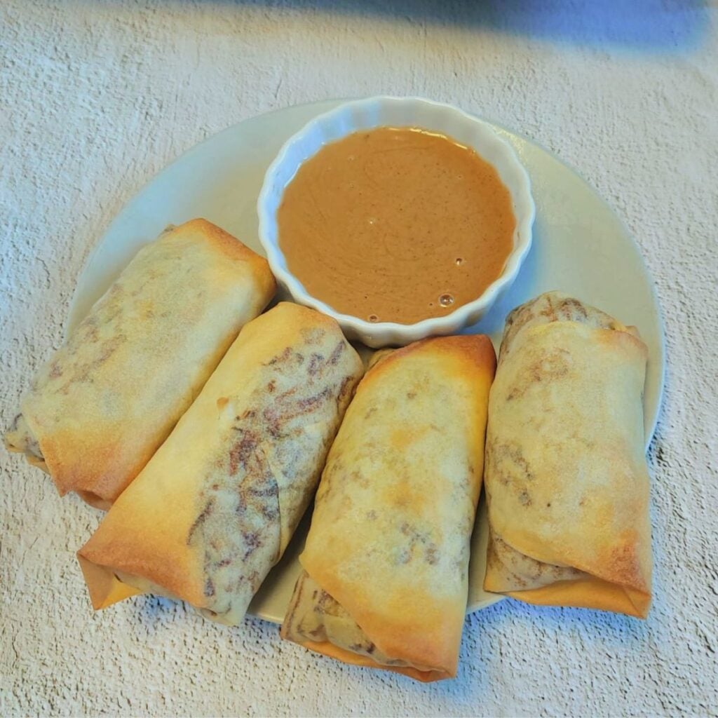 4 baked spring rolls on a plate with a bowl of brown dipping sauce.