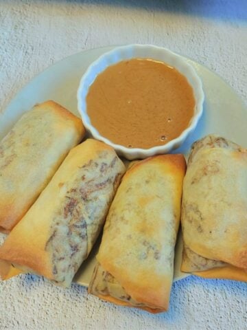 4 baked spring rolls on a plate with a bowl of brown dipping sauce.