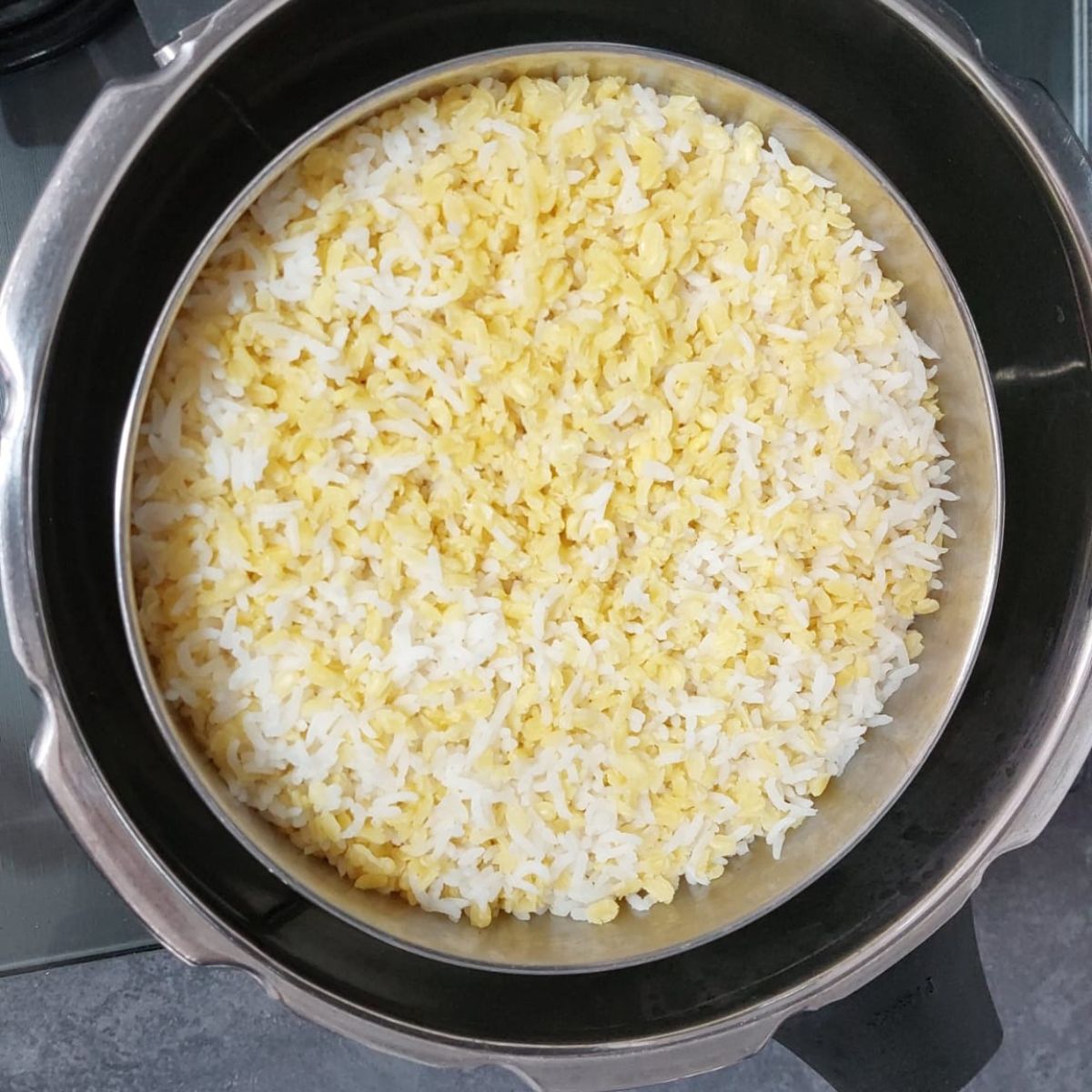 cooked rice and yellow lentils in a steel container placed inside the cooker.