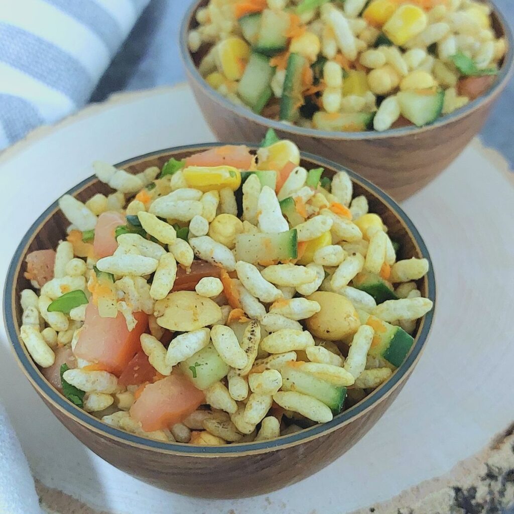 wooden bowls of puffed rice vegetable salad placed on a wooden board with a stripped napkin next to it.