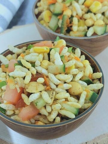 wooden bowls of puffed rice vegetable salad placed on a wooden board with a stripped napkin next to it.