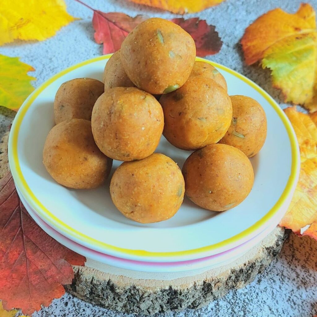 front view of stacked pumpkin energy balls on white plate placed on wooden block with fall leaves surrounding it.
