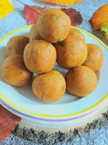 front view of stacked pumpkin energy balls on white plate placed on wooden block with fall leaves surrounding it.