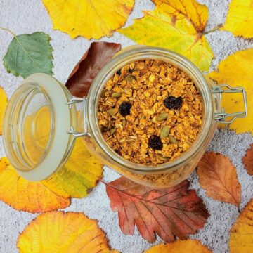 jar of pumpkin granola placed over autumn leaves with lid open.