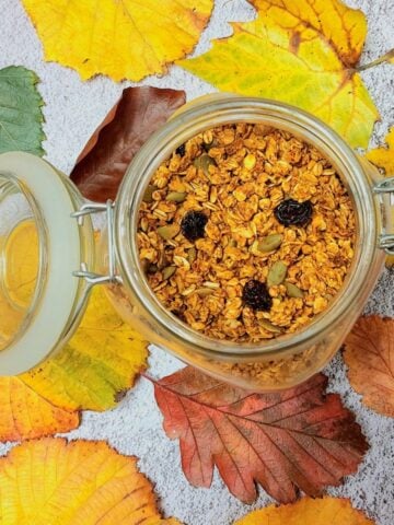 jar of pumpkin granola placed over autumn leaves with lid open.