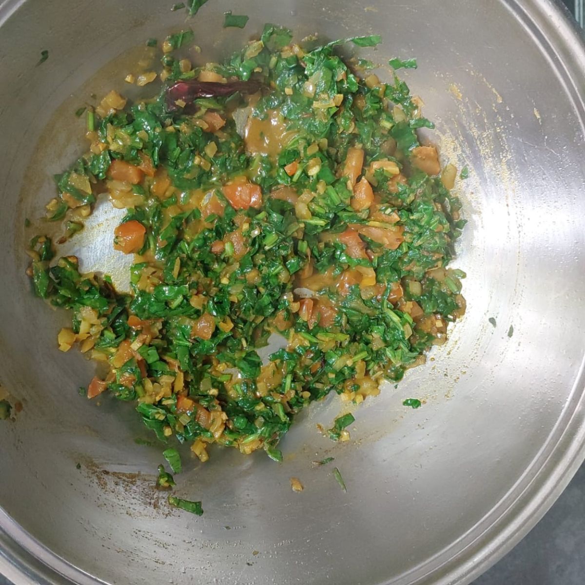 cooking spinach with tomatoes and spices in a wide steel pan.