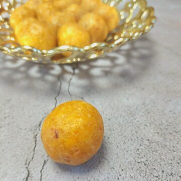 apricot energy ball placed on grey sheet with a golden bowl filled with yellow balls.