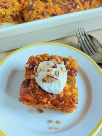 top view of slice of pumpkin baked oatmeal with yogurt nut topping on white plate with cutlery next to them.
