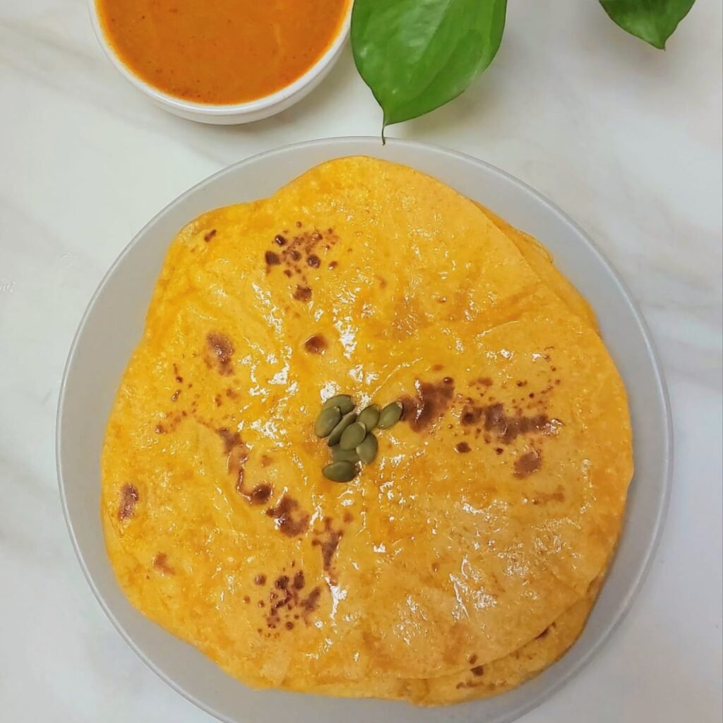 stack of pumpkin parathas on grey plate placed on marble along with a bowl of gravy