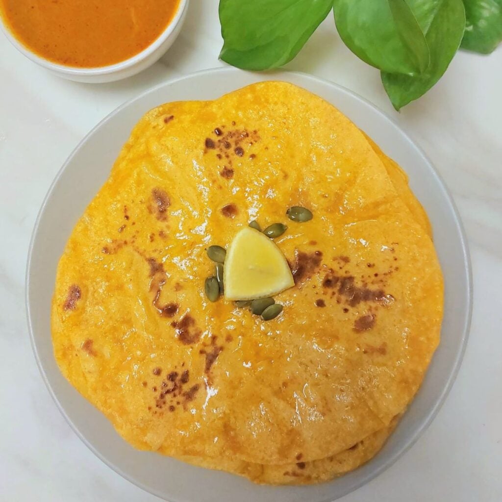 grey plate of stack of pumpkin parathas topped with lemon wedge placed on marble.