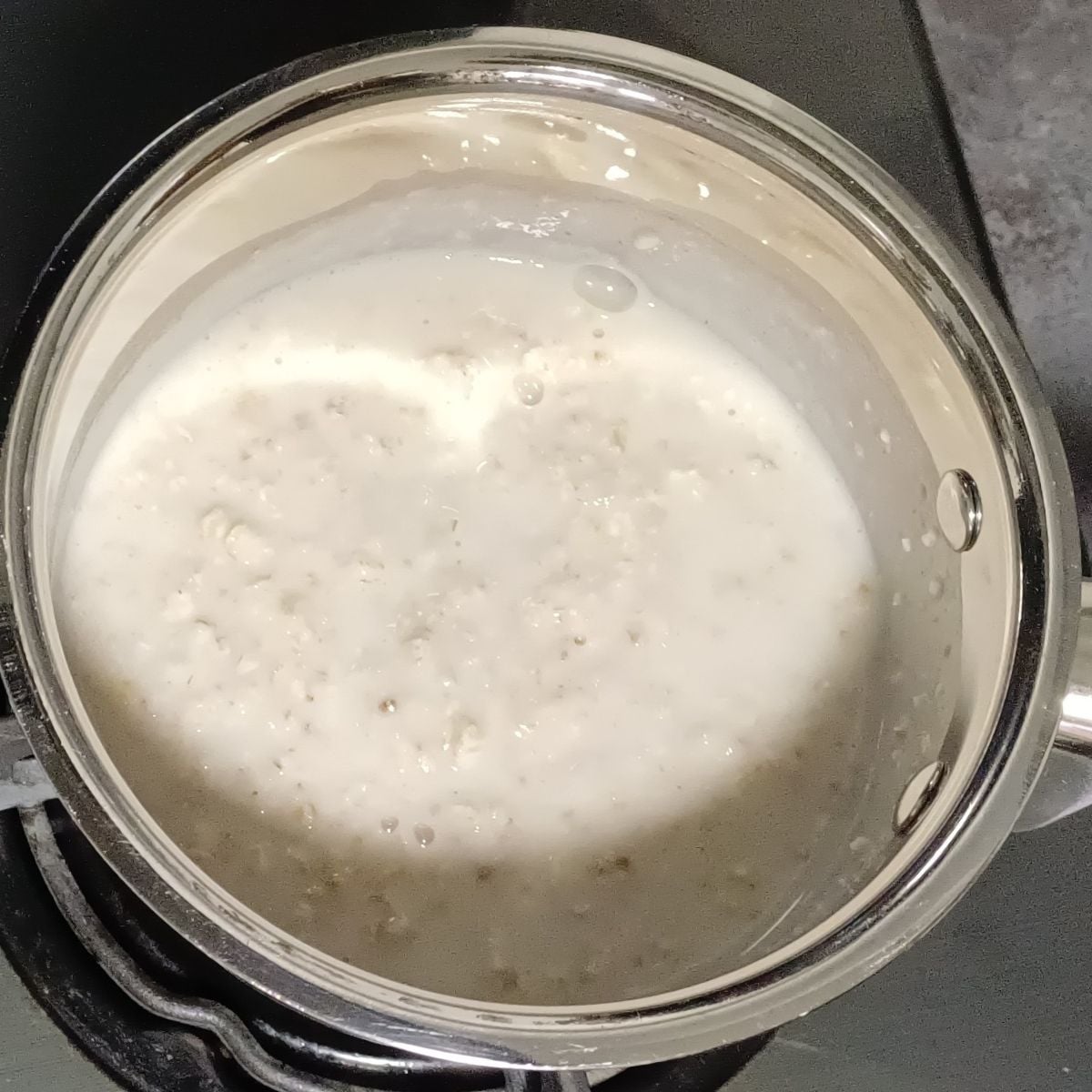 cooking oats with milk in a steel pan on stovetop.