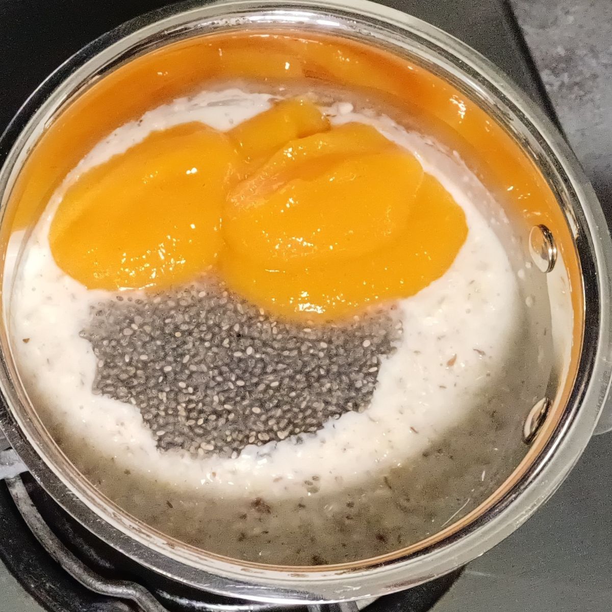cooked oats topped with soaked chia seeds and persimmon puree in a steel pan.