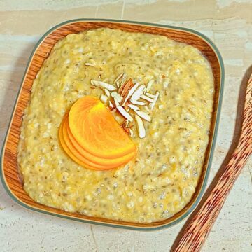 wooden bowl of persimmon oats chia porridge placed on a tile along with a wooden spoon next to it.
