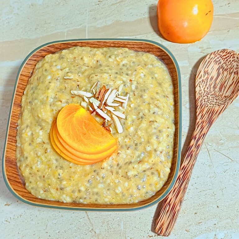 persimmon oats porridge in a square shaped wooden bowl topped with slivered almonds and persimmon slices.