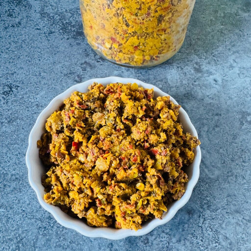 white bowl of nellikai thokku placed on textured tile along with a bottle of thokku behind it.