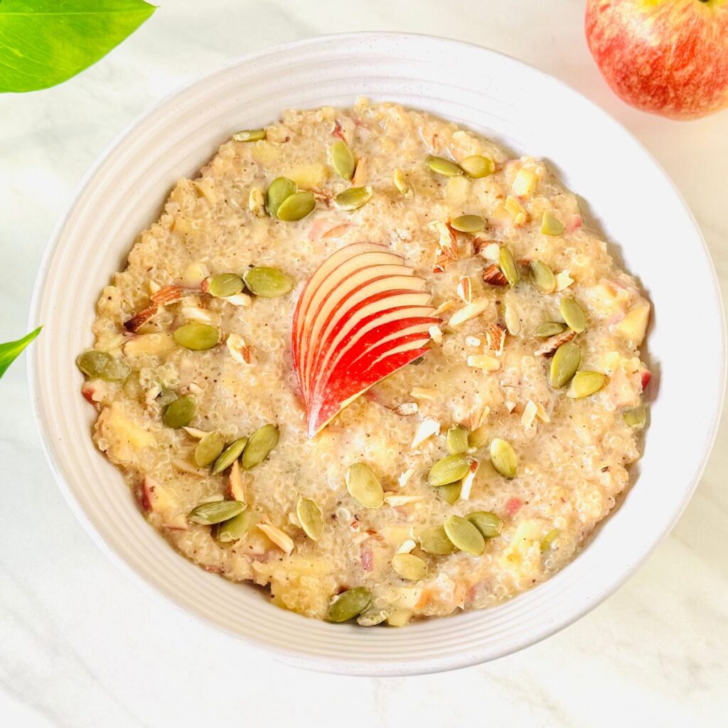 white bowl of quinoa apple porridge topped with apple slices and nuts