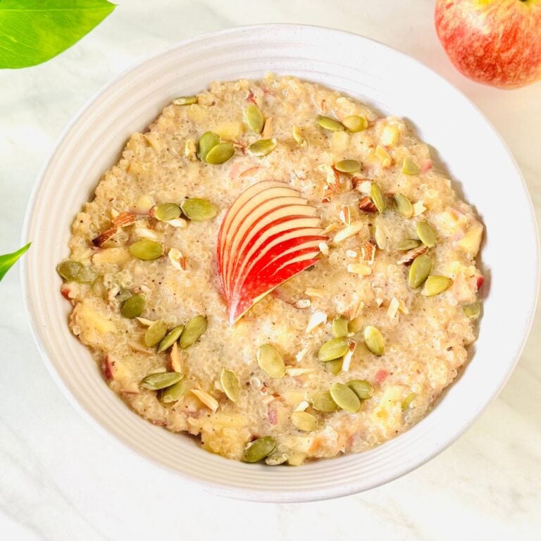 white bowl of quinoa apple porridge topped with apple slices and nuts