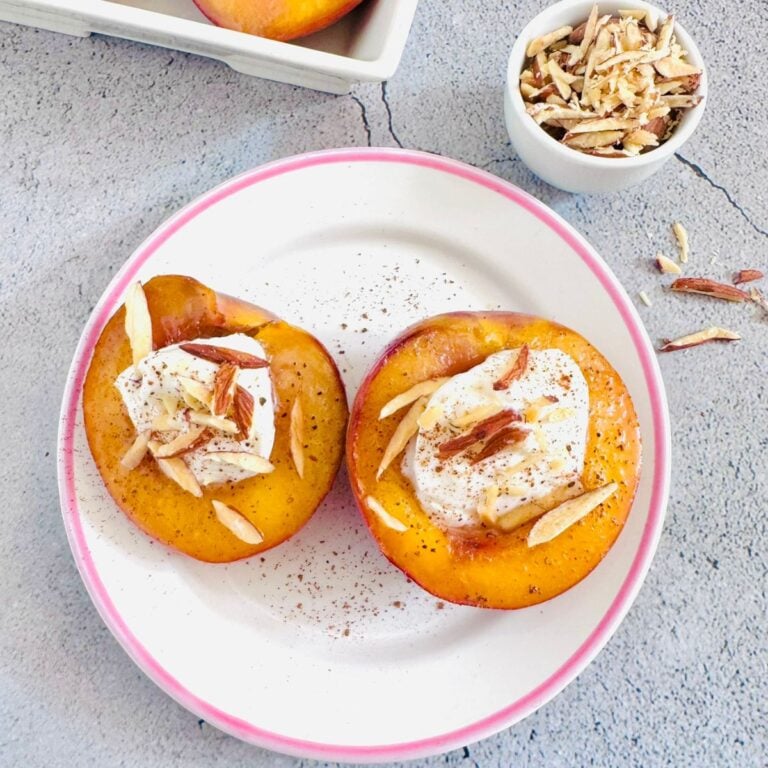 two halves of caramelised nectarines on a white plate placed on a granite along with a pinch bowl of almonds and a plate of nectarines