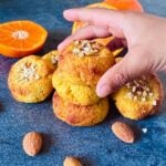 child picking orange almond cookie from a stack placed on a granite along with cut oranges.