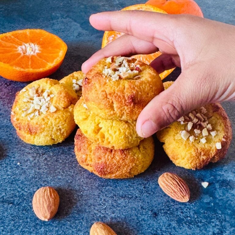 child picking orange almond cookie from a stack placed on a granite along with cut oranges.