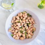top view of a bowl of butter bean salad with garlic herb dressing placed on white marble along with a glass of water with lemon slice.