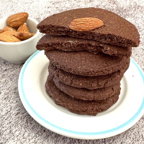 stack of kid friendly almond chocolate cookies placed on a white plate with a broken cookie on top.
