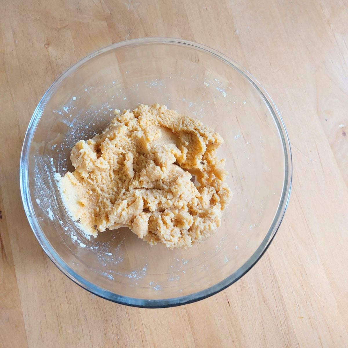 glass bowl of almond orange mixture placed on wooden table.