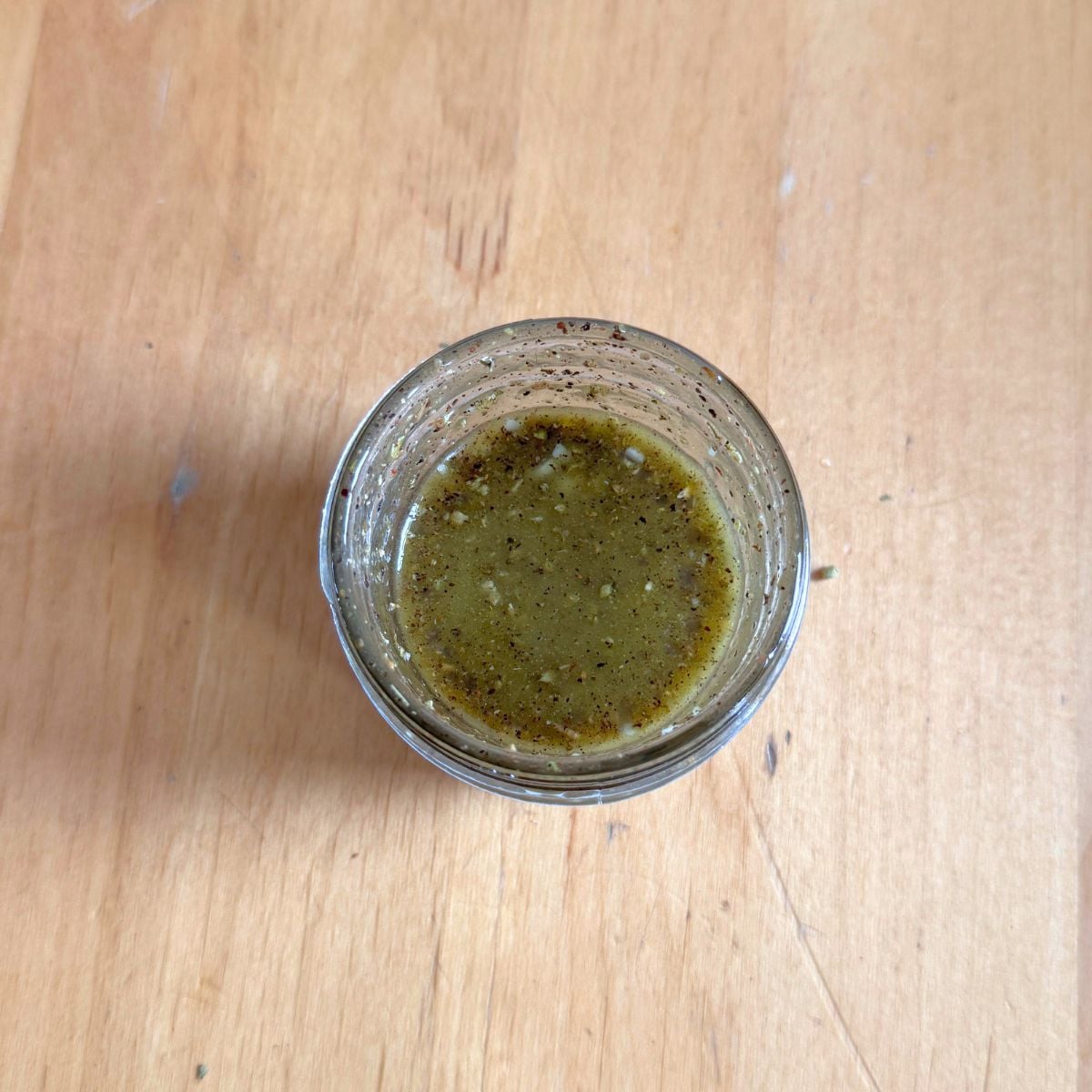 glass jar of olive oil garlic herb dressing on wooden table.