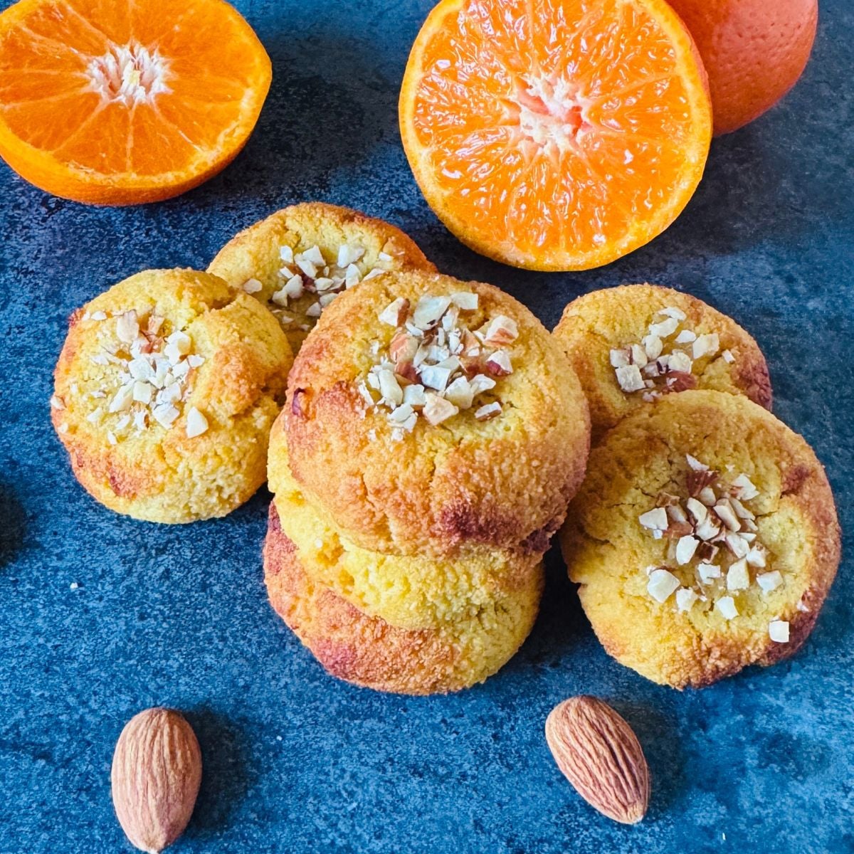 stack of gluten free kid friendly 3 ingredient orange almond cookies placed on granite along with half cut oranges.