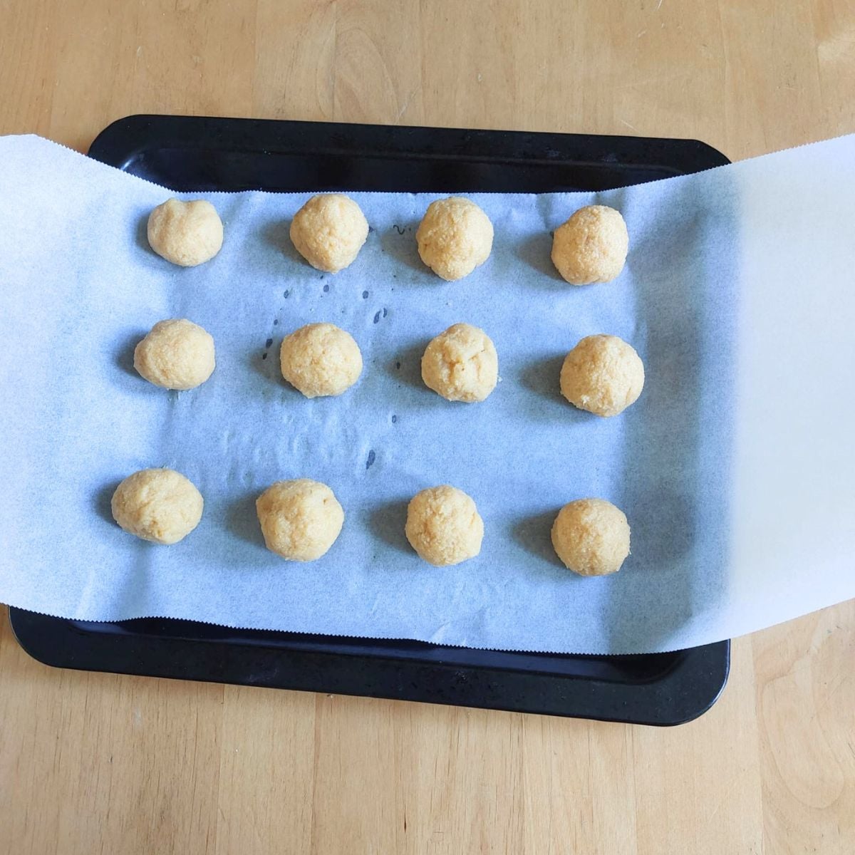 almond orange balls on lined baking sheet placed on wooden table.