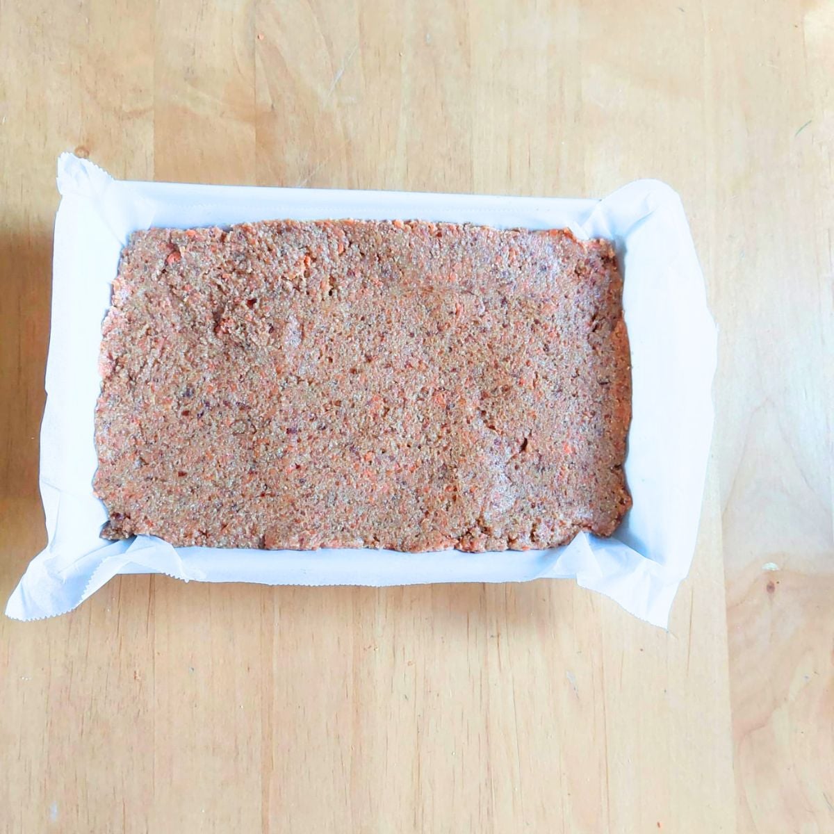 carrot date oatmeal mixture in a lined baking dish ready to go in the oven.