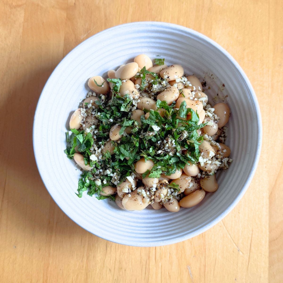 white bowl of butter beans topped with garlic herb dressing placed on wooden table.