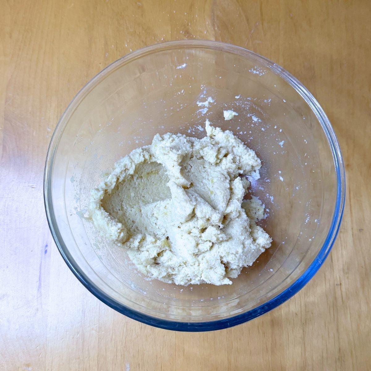 glass bowl of almond banana cookie dough placed on wooden table.